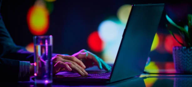 Anonymous writer typing on laptop with neon light — symbolizing pseudonymous authorship in 2026